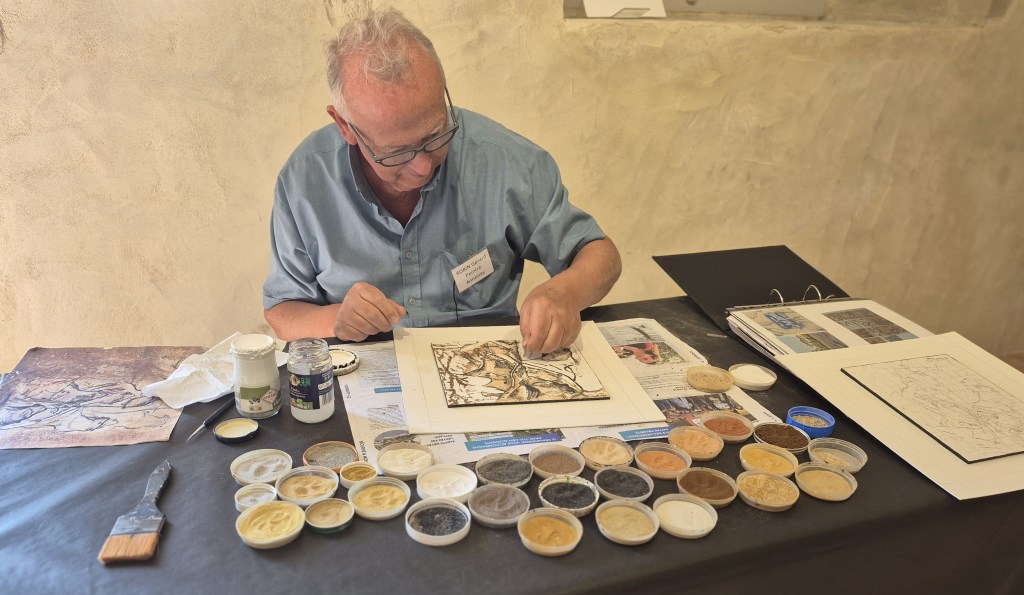Gérard Robin à l'œuvre dans son atelier d'Annonay. Devant lui, les coupelles de sables naturels du monde entier qui composent sa palette